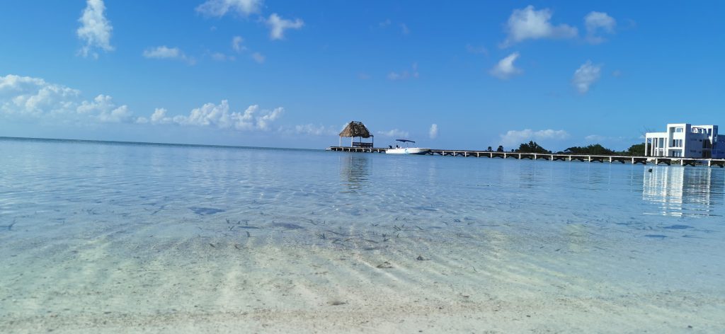 Shallow calm acqua waters with a palapa and boat in the background