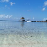 Shallow calm acqua waters with a palapa and boat in the background
